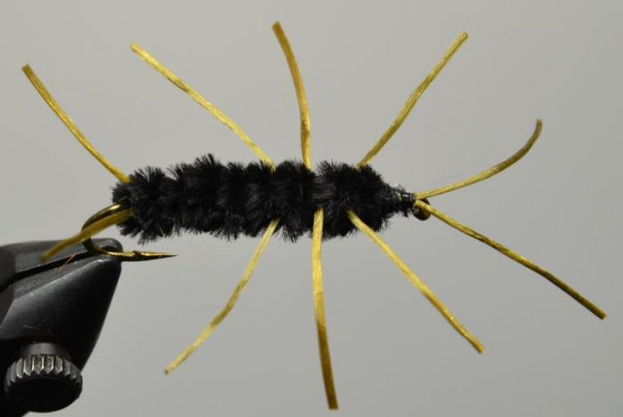 Black Pat's Rubber Legs fly pattern with gold legs held in a vise for fly tying.